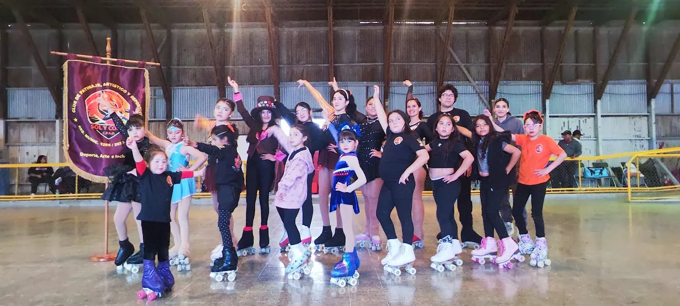 Deportistas y equipo del club posando con sus patines en una pista cubierta de estructura de madera y muros de calamina, junto al estandarte de Sol y Cobre.